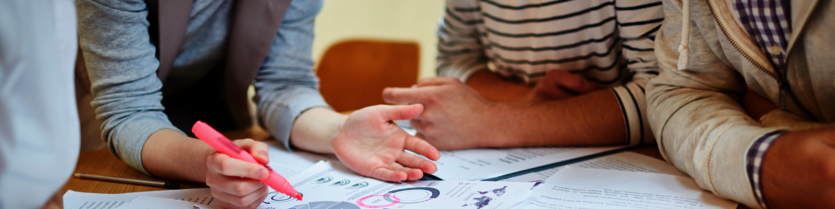 Close up view of hands collaborating on a project at a desk.